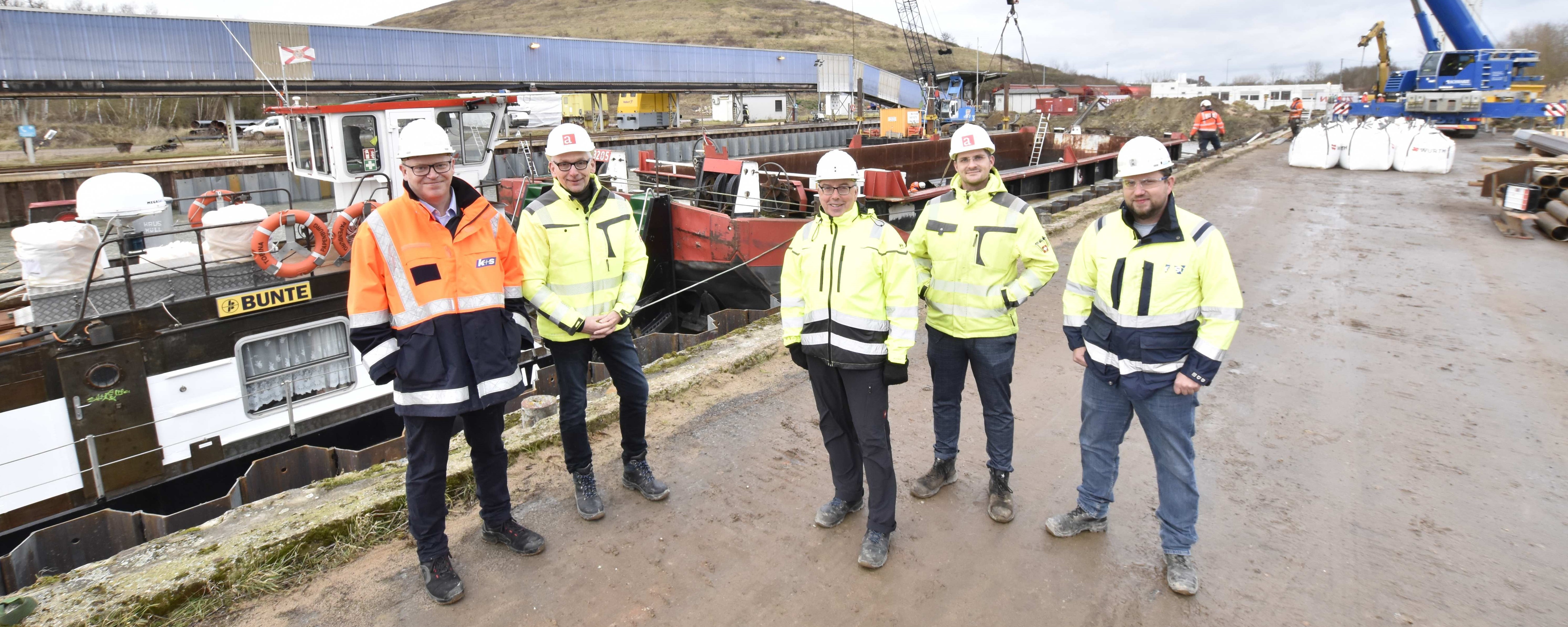 Das Projektteam: (v.l.n.r.) Tim Warncke, Christian Lindner (Ingenieurbüro Assmann), Holger Illian, Pascal Weiss (Ingenieurbüro Assmann), Jochen Meyer. Im Hintergrund ist die hellblaue Verladebrücke und die abgedeckte Halde Friedrichshall zu sehen.