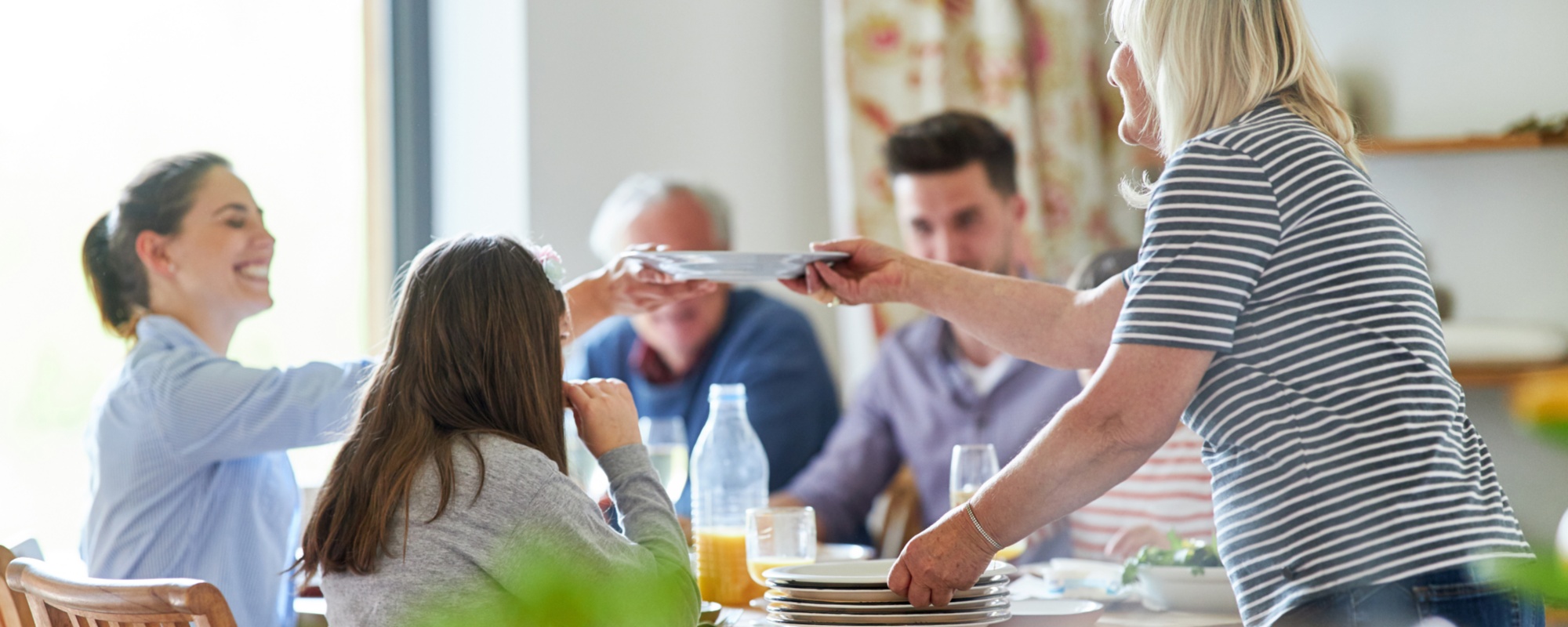 Family sitting at the dining table for a meal together and arranging brightly colored plates